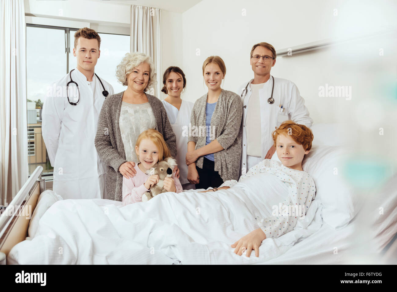 Doctors and famiy in hospital standing by bed of sick boy Stock Photo