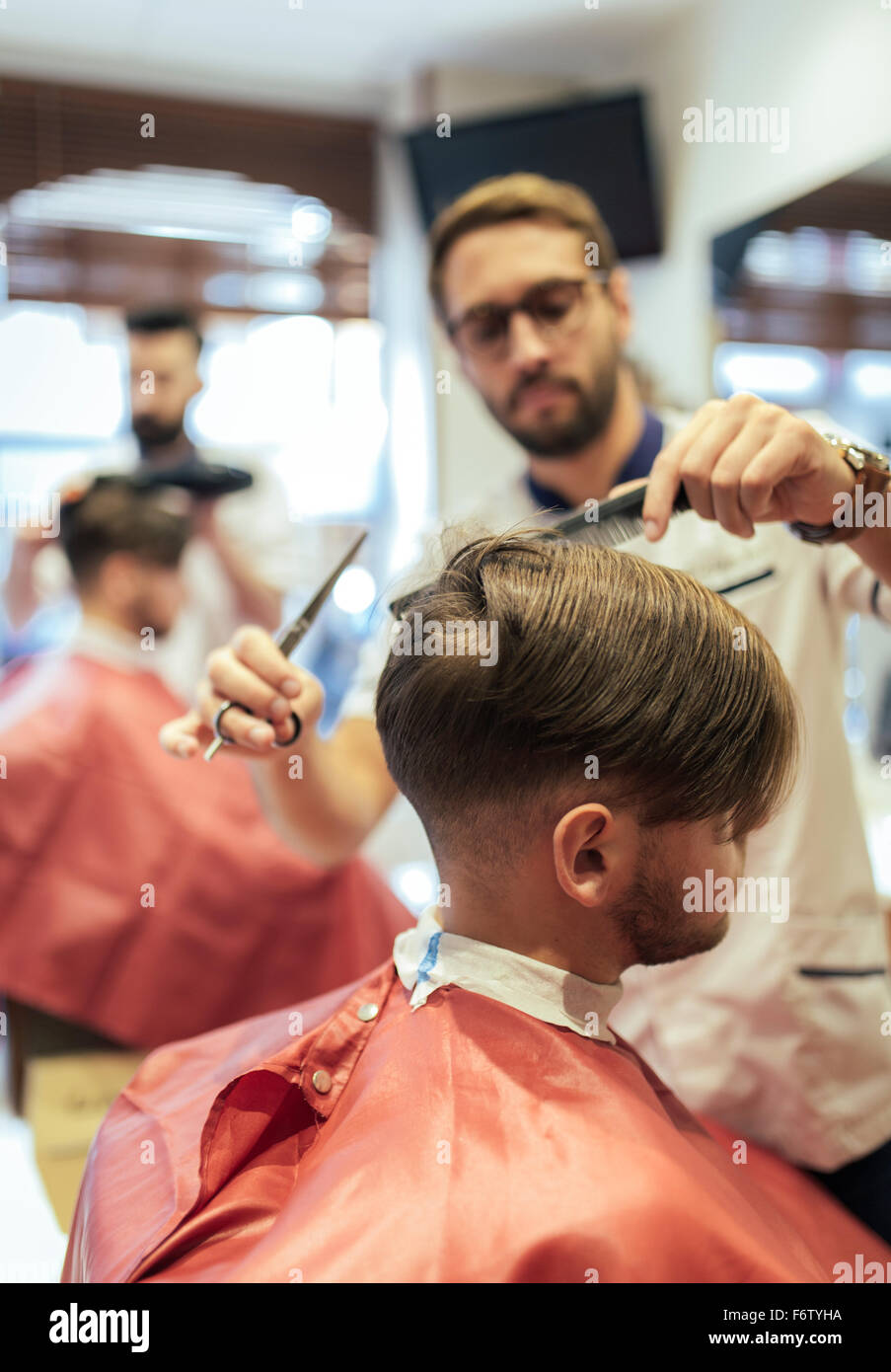Barber cutting hair of a customer with twin brother in background Stock