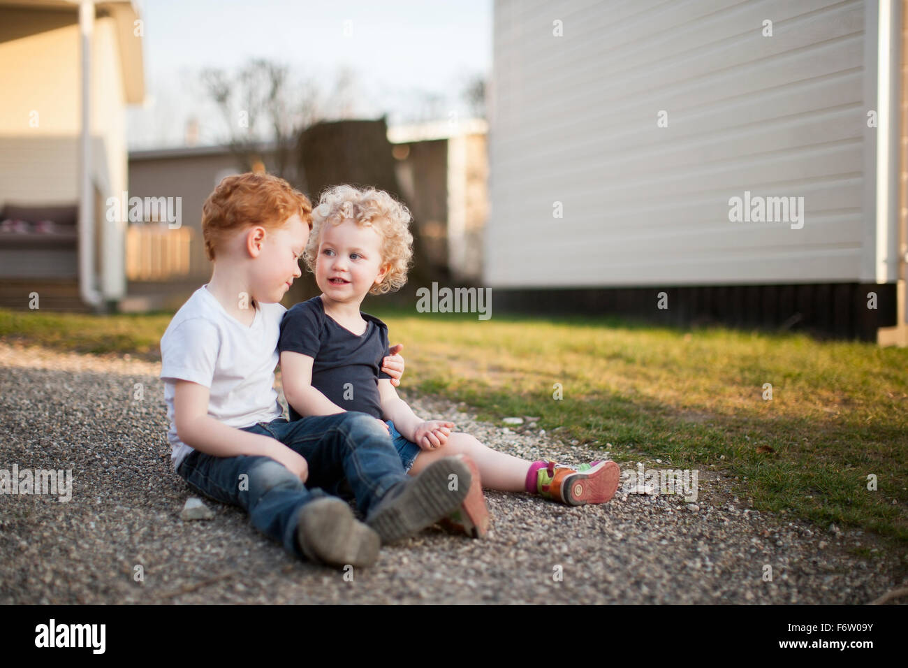 Little girl and boy sitting on gravel path Stock Photo