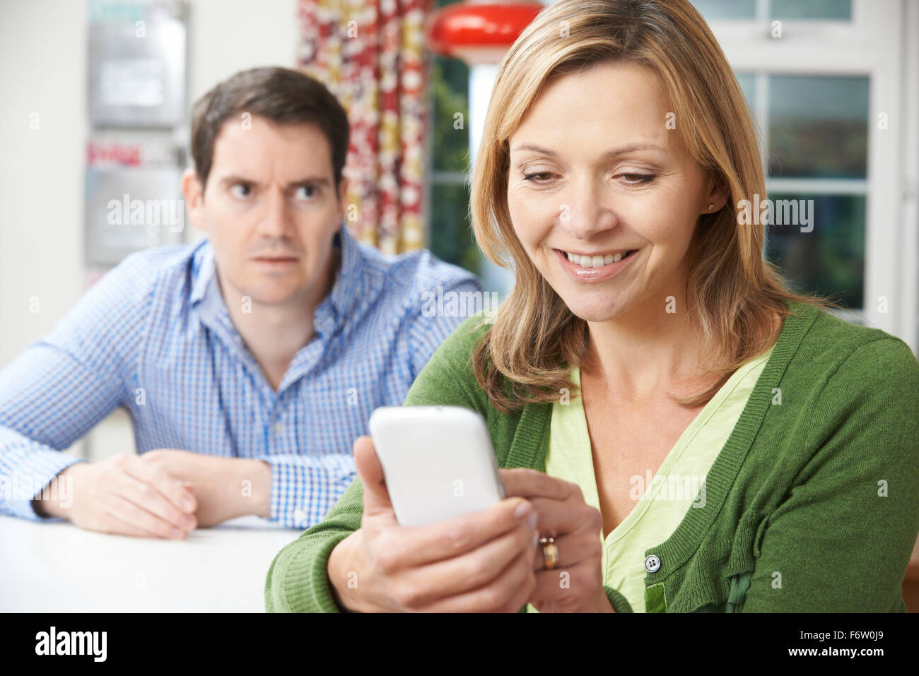 Unhappy Man Sitting At Table As Partner Texts On Mobile Phone Stock Photo