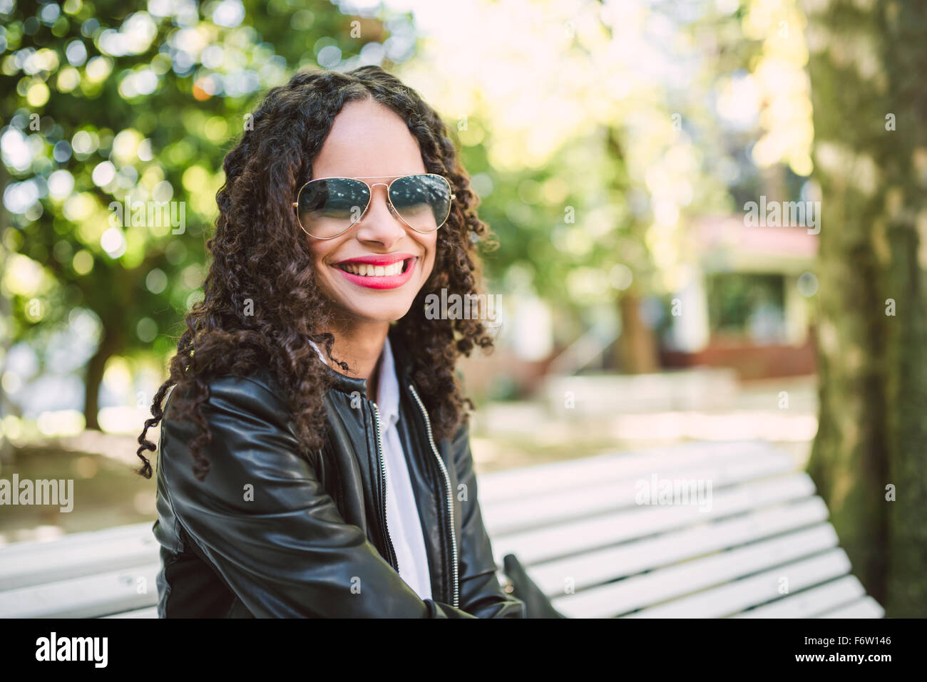Portrait of smiling woman wearing sunglasses and leather jacket sitting ...