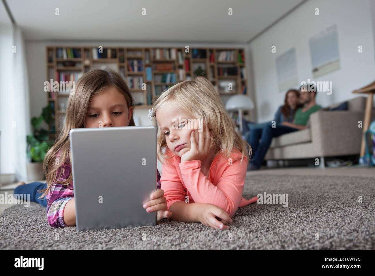 Two little sisters lying on the floor at living room with digital ...