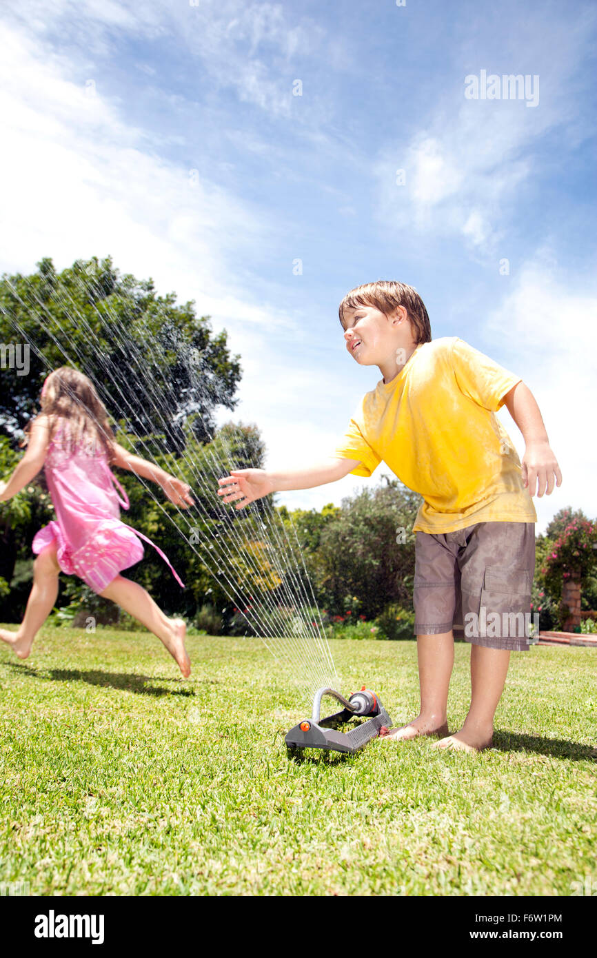 Two little children playing with lawn sprinkler in the garden Stock