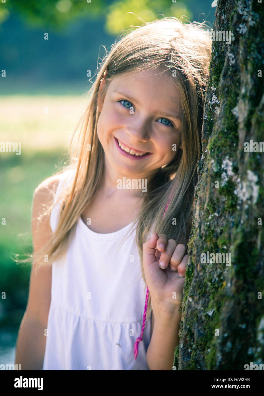 Portrait of smiling little girl leaning against tree trunk Stock Photo ...