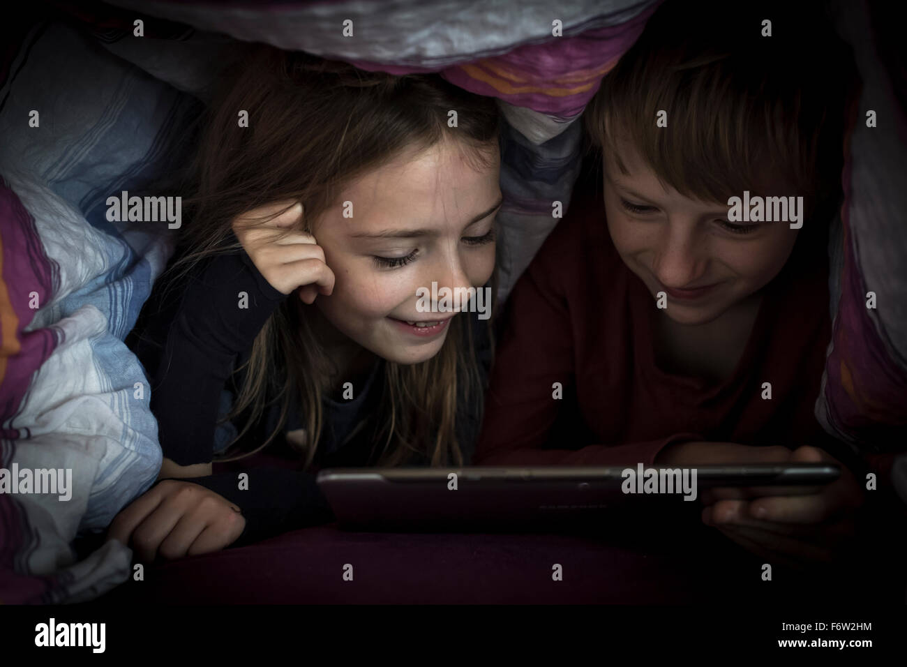 Brother and sister lying side by side using digital tablet under a ...