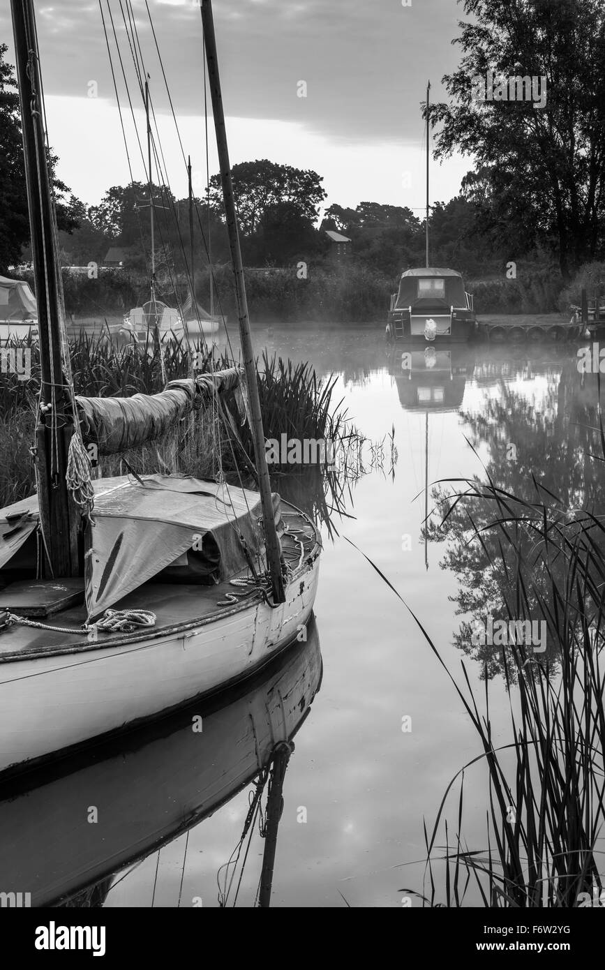 Sailing boats moored on riverbank at sunrise in countryside landscape in black and white Stock Photo