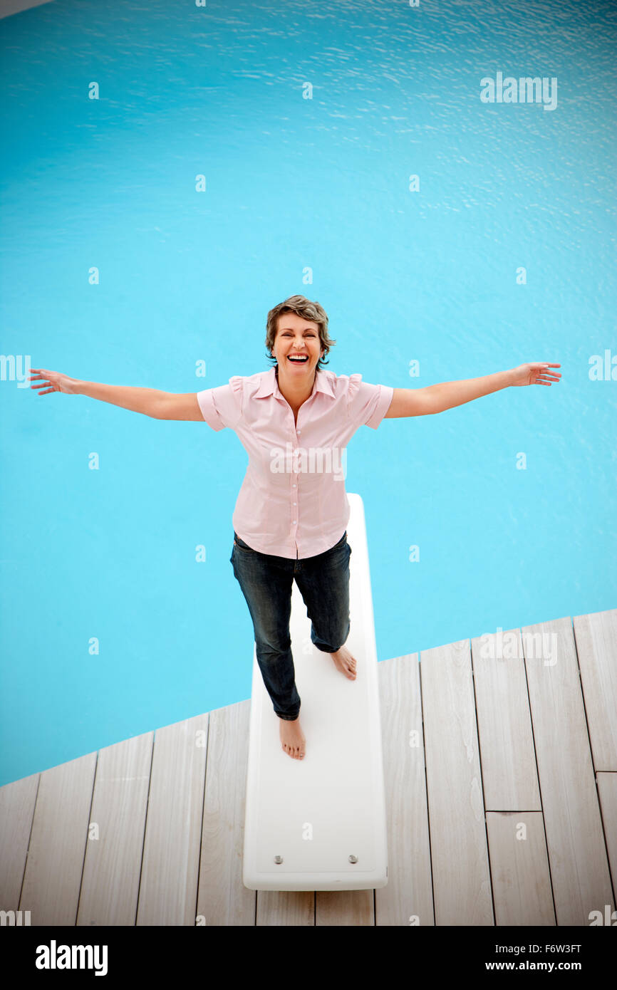 Portrait of happy woman standing on springboard with arms outstretched ...