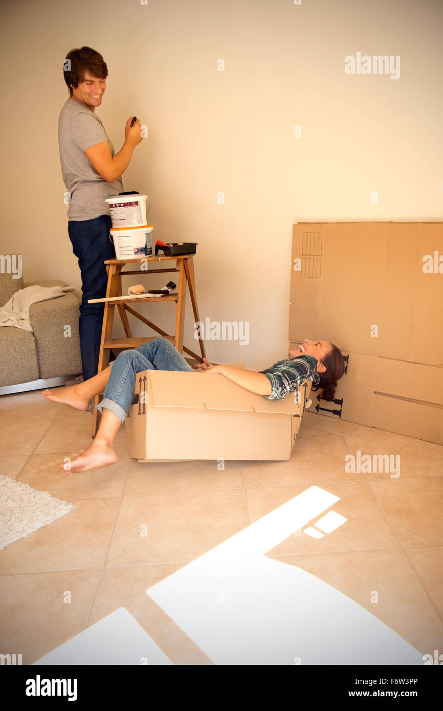 Laughing woman in cardboard box with man painting wall Stock Photo - Alamy