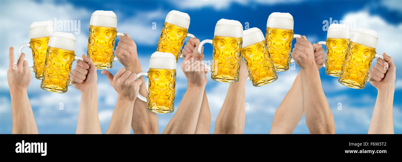 many hands holding german oktoberfest beer on blue cloudy sky Stock Photo