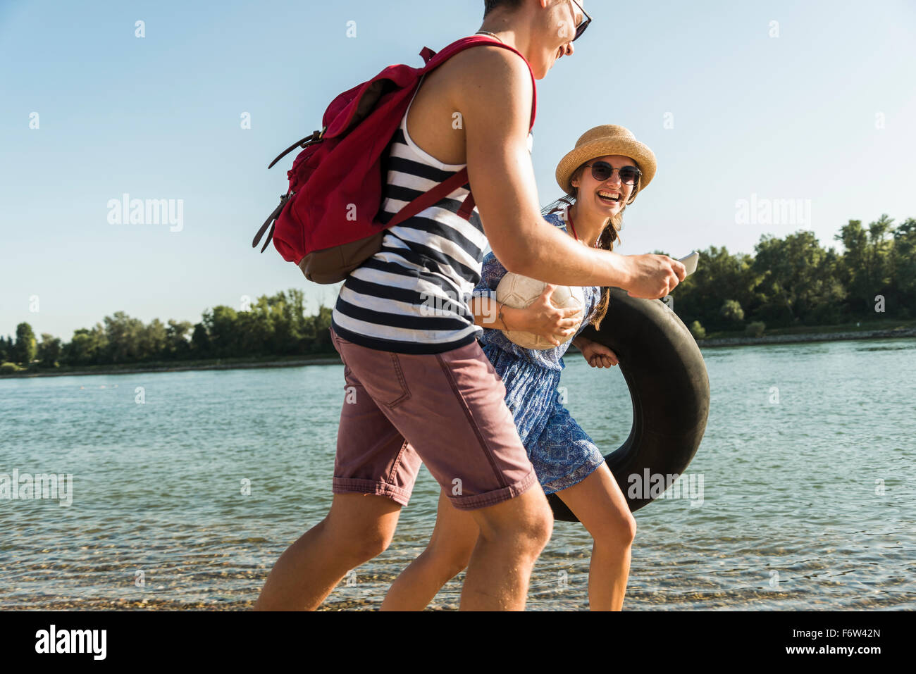 Young couple with inner tube and cell phone walking at the riverside Stock Photo