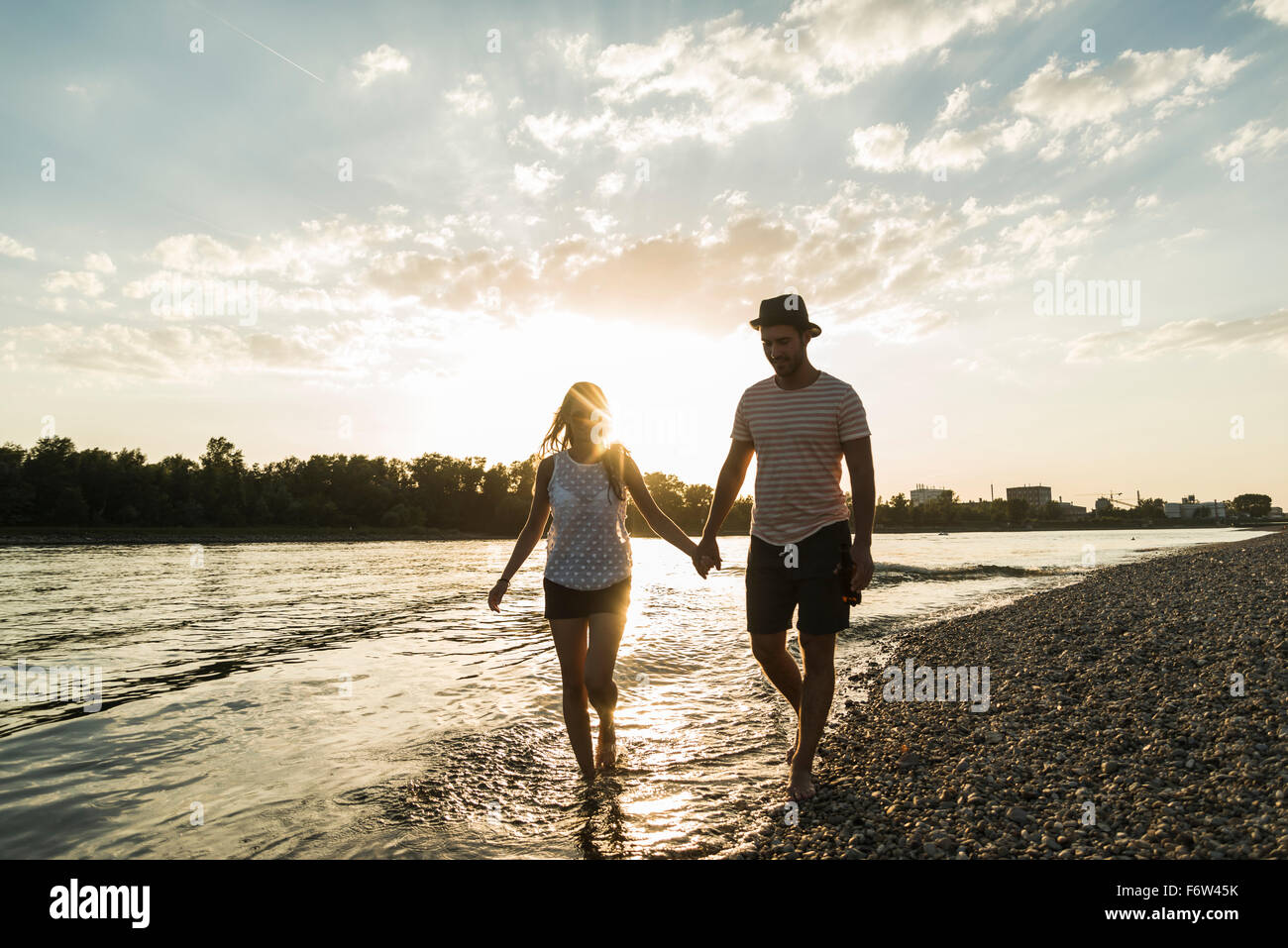 Couple walking hand in hand at the riverside at sunset Stock Photo