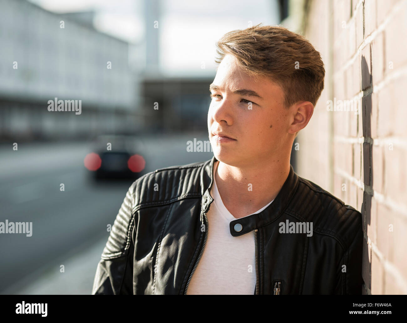 Young man leaning against brick wall looking around Stock Photo - Alamy