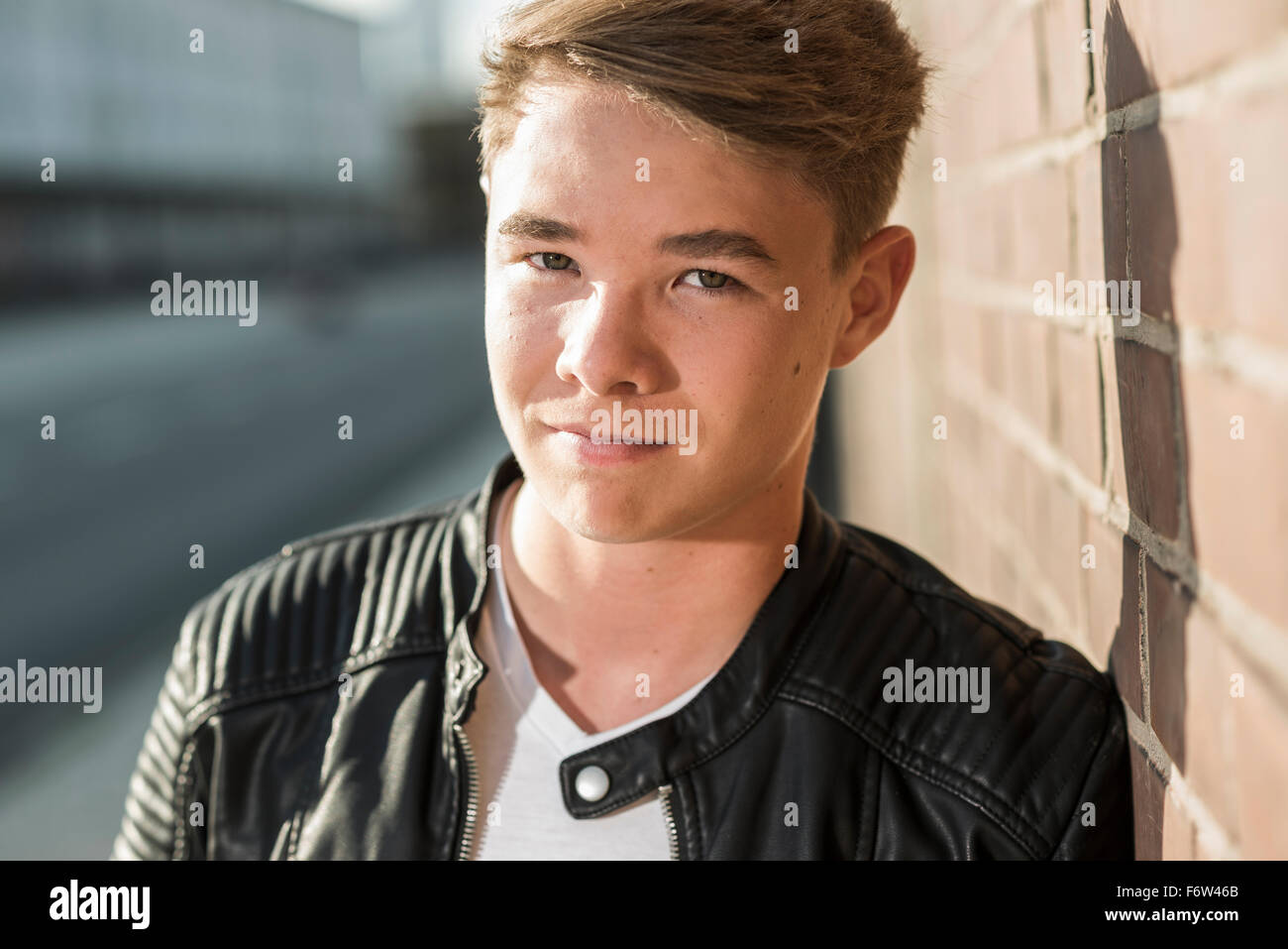 Portrait of young man leaning against brick wall Stock Photo - Alamy