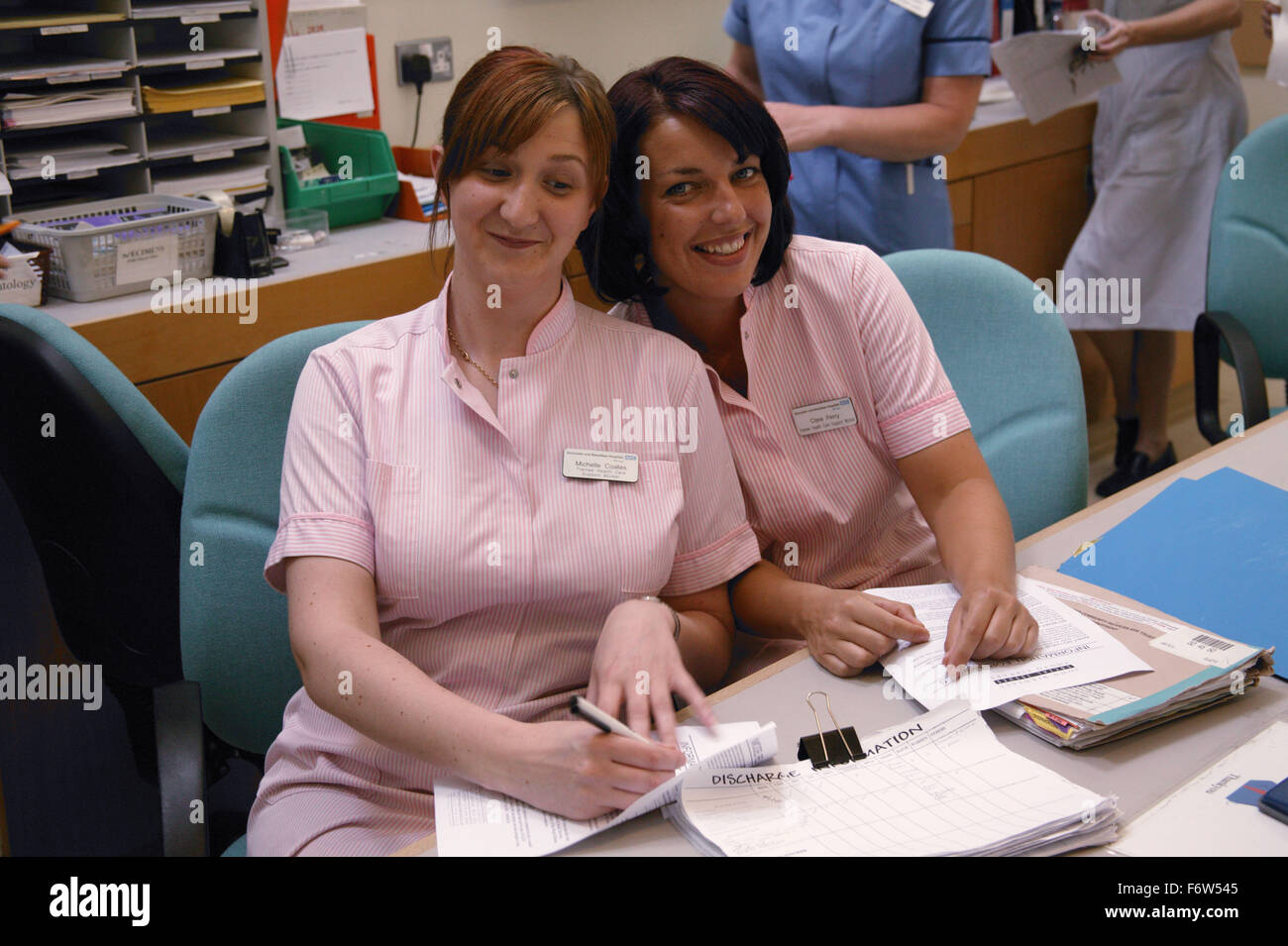 Two trainee healthcare workers sitting behind hospital desk smiling, Stock Photo