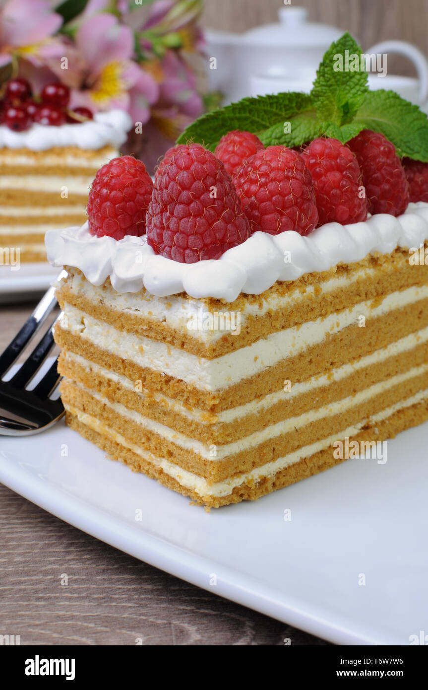 Piece of honey cake with whipped cream and raspberries Stock Photo