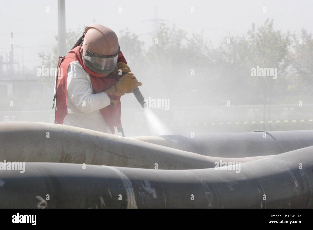 A worker uses high-pressure grit blasting to clean petrochemical pipes Stock Photo