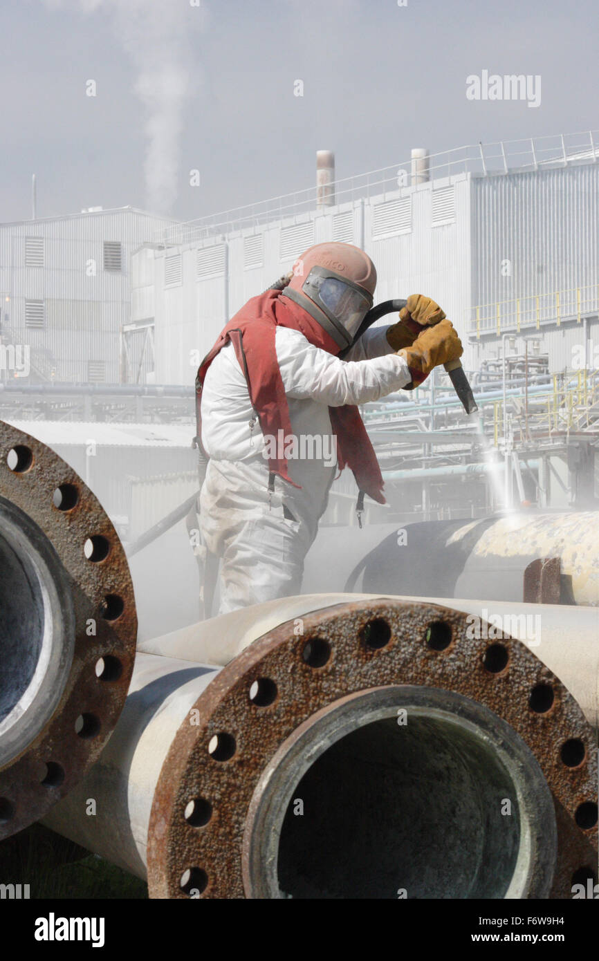 A worker uses high-pressure grit blasting to clean petrochemical pipes Stock Photo