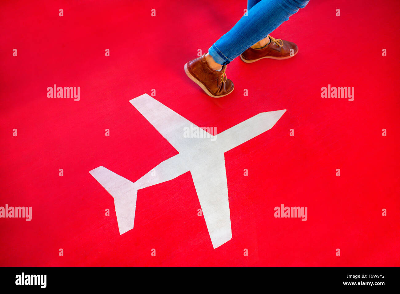 Airplane sign with female legs walking on the red floor. Departure concept Stock Photo