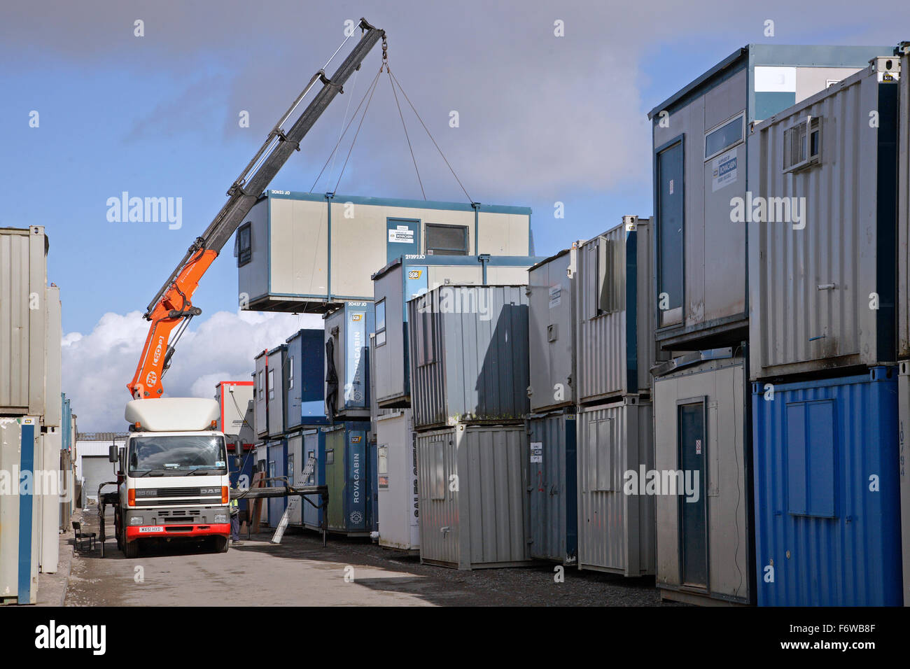 A site cabin is lifted onto a truck from a stack of cabins and containers in an outdoor yard Stock Photo