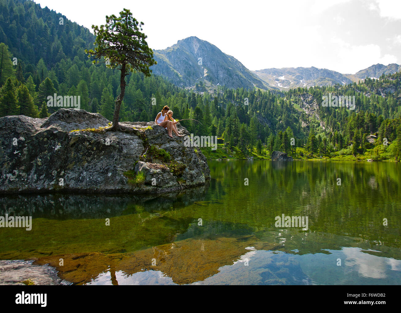 Young people sitting on a rock at lake Dieslingsee, Turracher Hoehe, Styria, Austria Stock Photo
