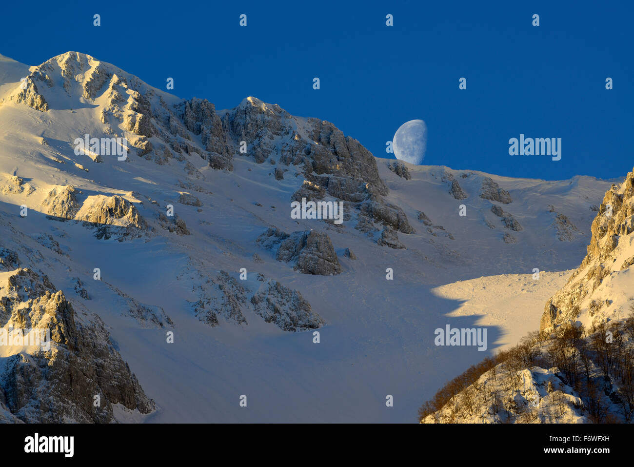 Moon standing above the snow-covered cirque at Monte Sirente, Valle Lupara, Monte Sirente, Abruzzi, Apennines, l' Aquila, Italy Stock Photo