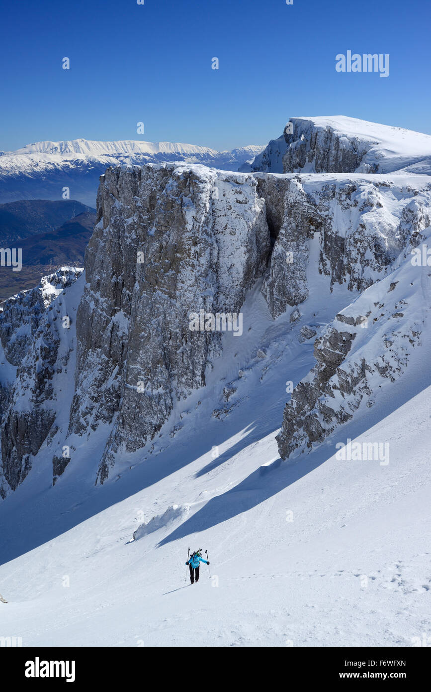 Female backcountry skier ascending through snow-covered cirque at Monte Sirente, Maiella range in background, Valle Lupara, Abru Stock Photo