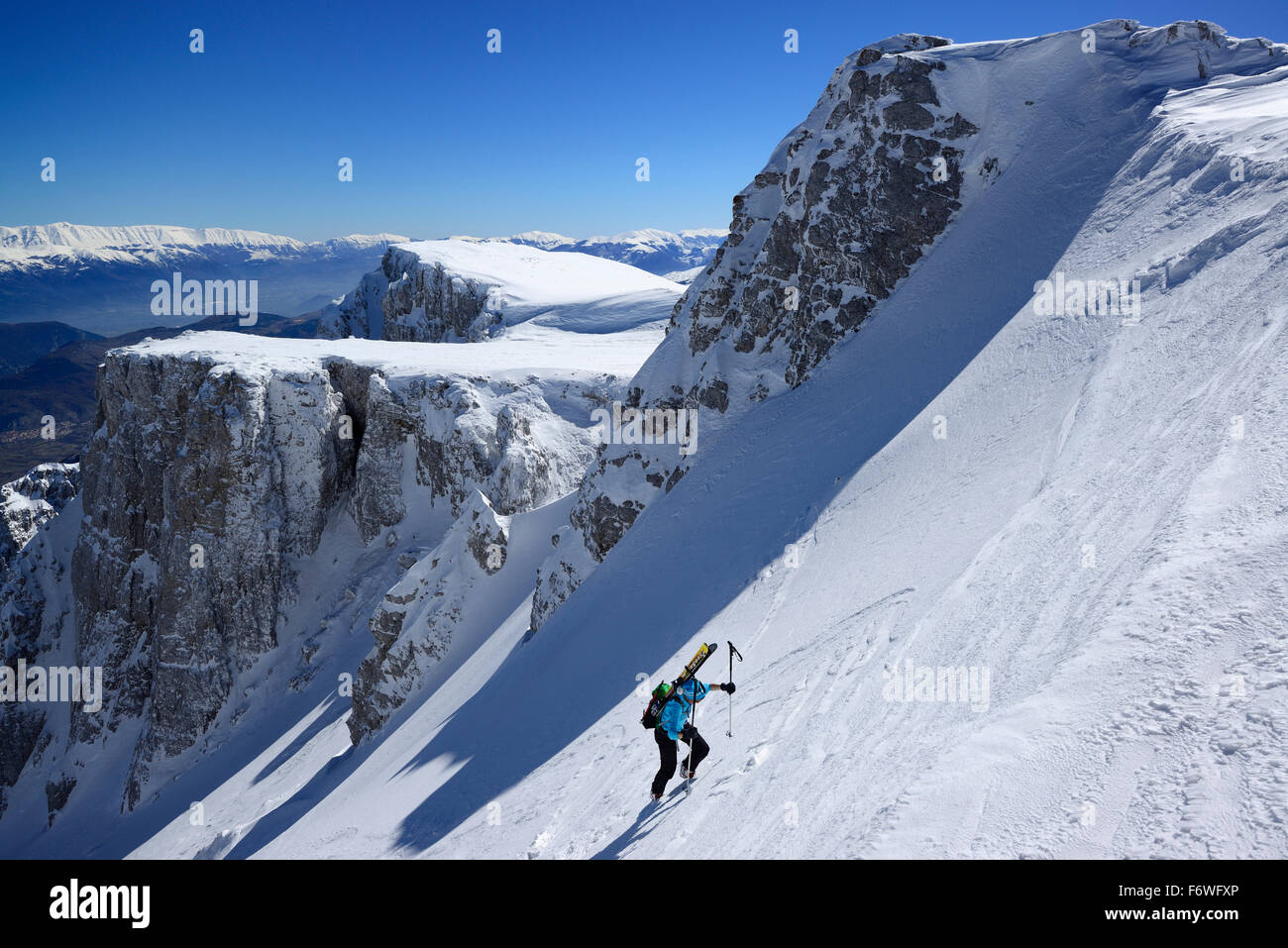 Female backcountry skier ascending through snow-covered cirque at Monte Sirente, Maiella range in background, Valle Lupara, Abru Stock Photo