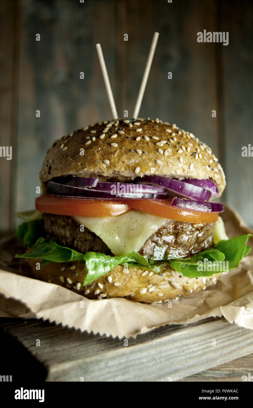 Gourmet burger with melted cheese, tomato and onion filling on top of a wooden chopping board Stock Photo