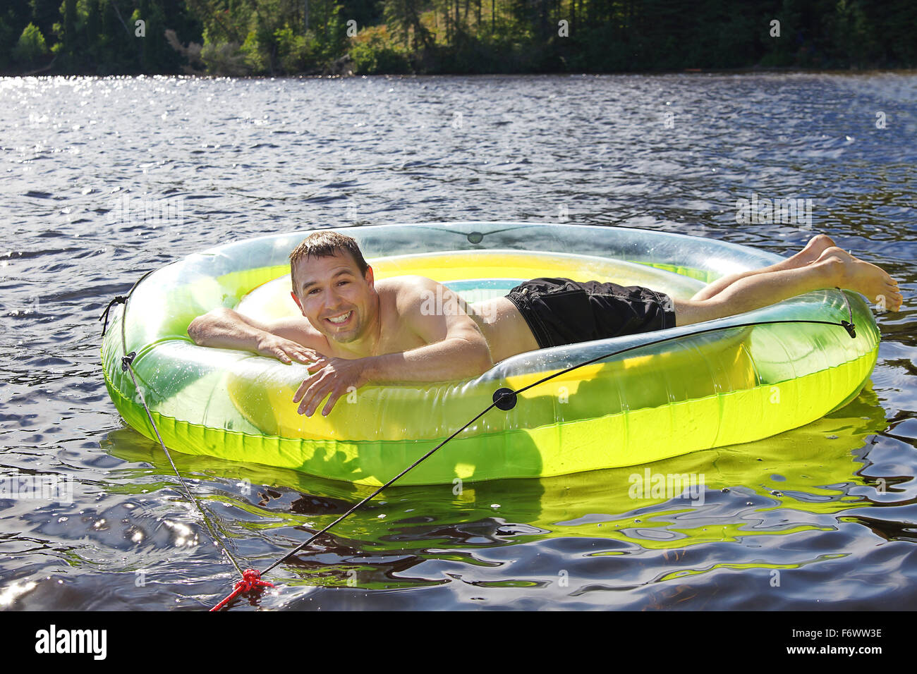 Man having fun and relaxing on large plastic buoy or swim ring at the lake Stock Photo