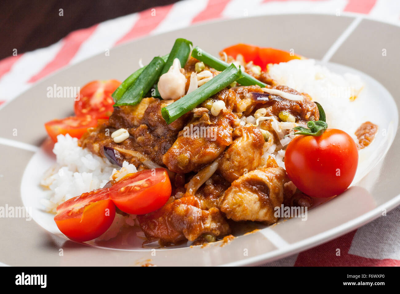 Szechuan chicken with white rice on a plate decorated with chive and cocktail tomato Stock Photo