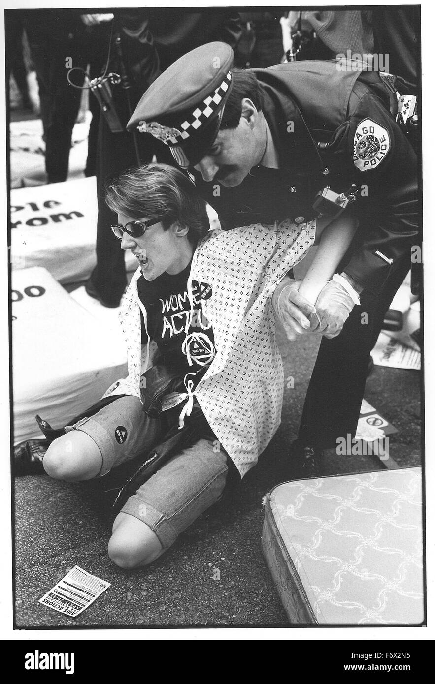 Chicago police arrest a female protester in the ACT UP (AIDS Coalition to Unleash Power) group in April 1990. The group was protesting at a number of sites around the city due to lack of funding for AIDS treatment. In this part of the protest, women created an 'AIDS Ward' in the street, using mattresses and sat down blocking traffic until they were arrested. The specific action targeted the problem that at the time, the Cook County Hospital would not accept female patients in their AIDS ward, despite having empty beds available. Stock Photo