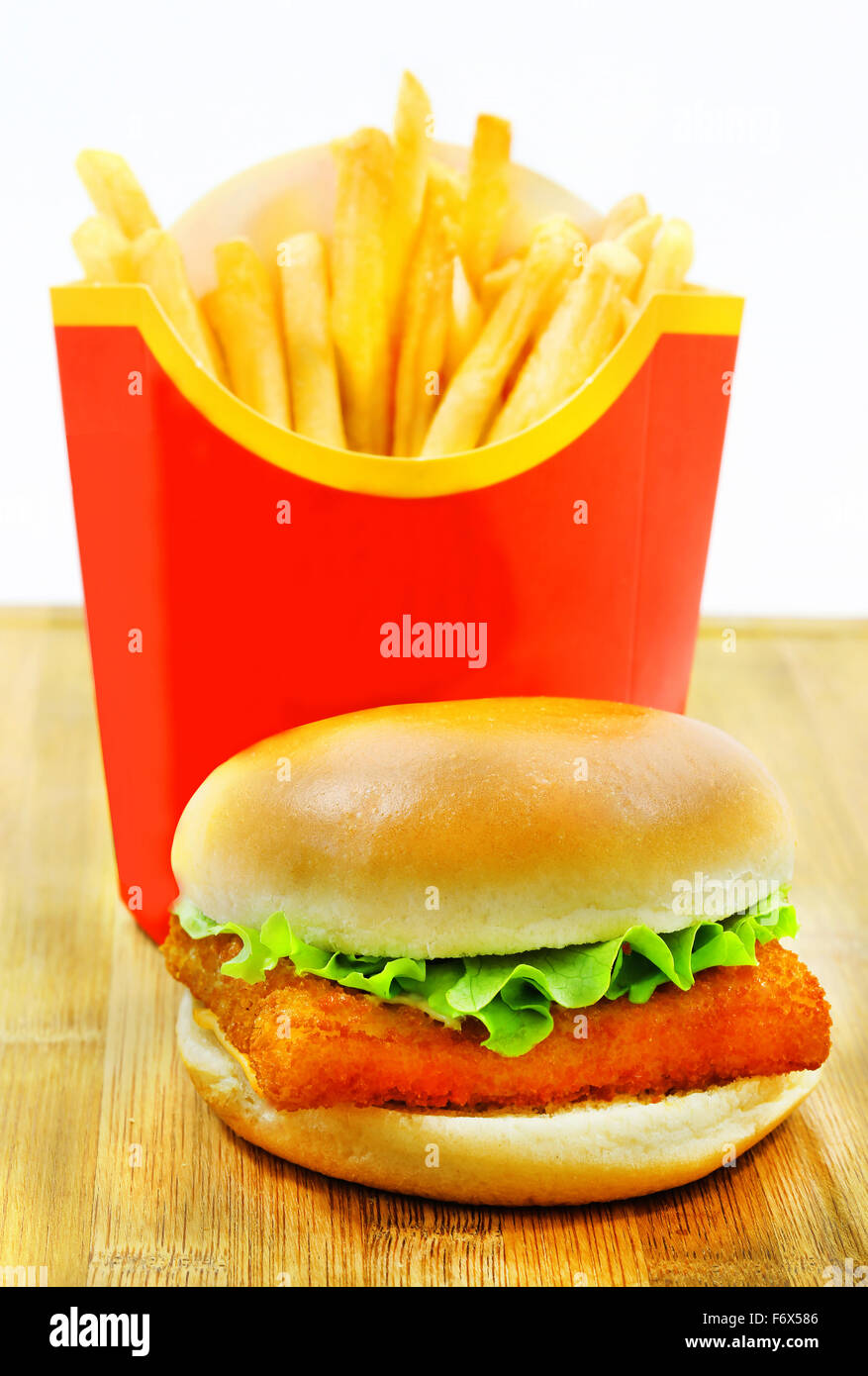 Burger with fries and fish is photographed close-up on a wooden board Stock Photo