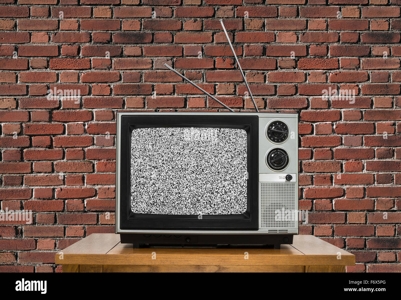 Old analogue television with static screen and brick wall. Stock Photo