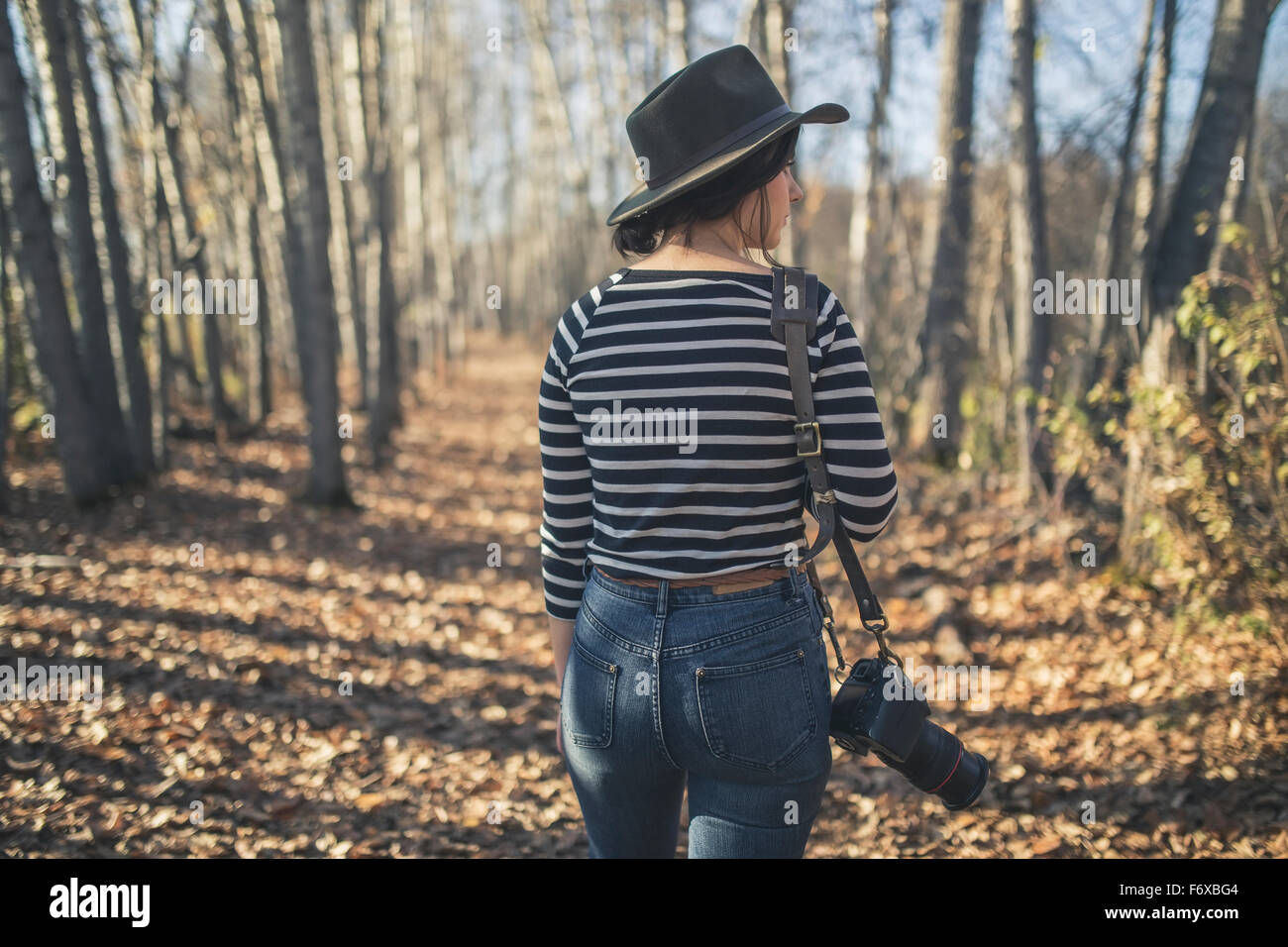 Young woman wearing hat with camera and walking through the woods near ...