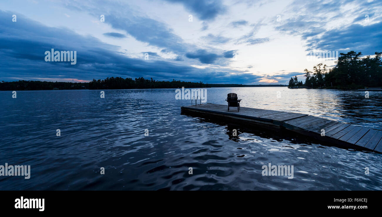 Silhouette of an adirondack chair on a wooden dock along a lake at ...