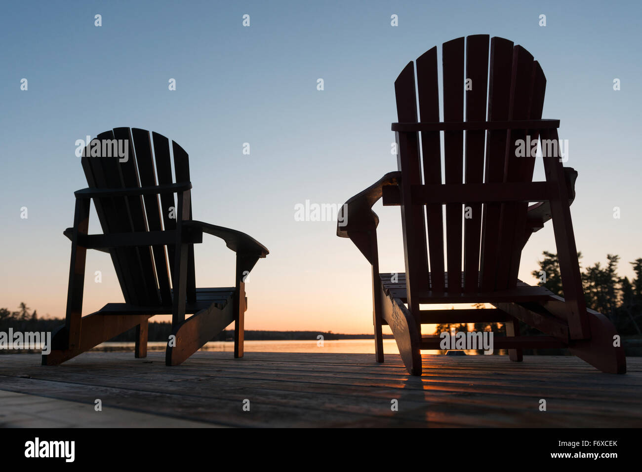 Silhouette of adirondack chairs on a wooden dock along a lake at sunset ...