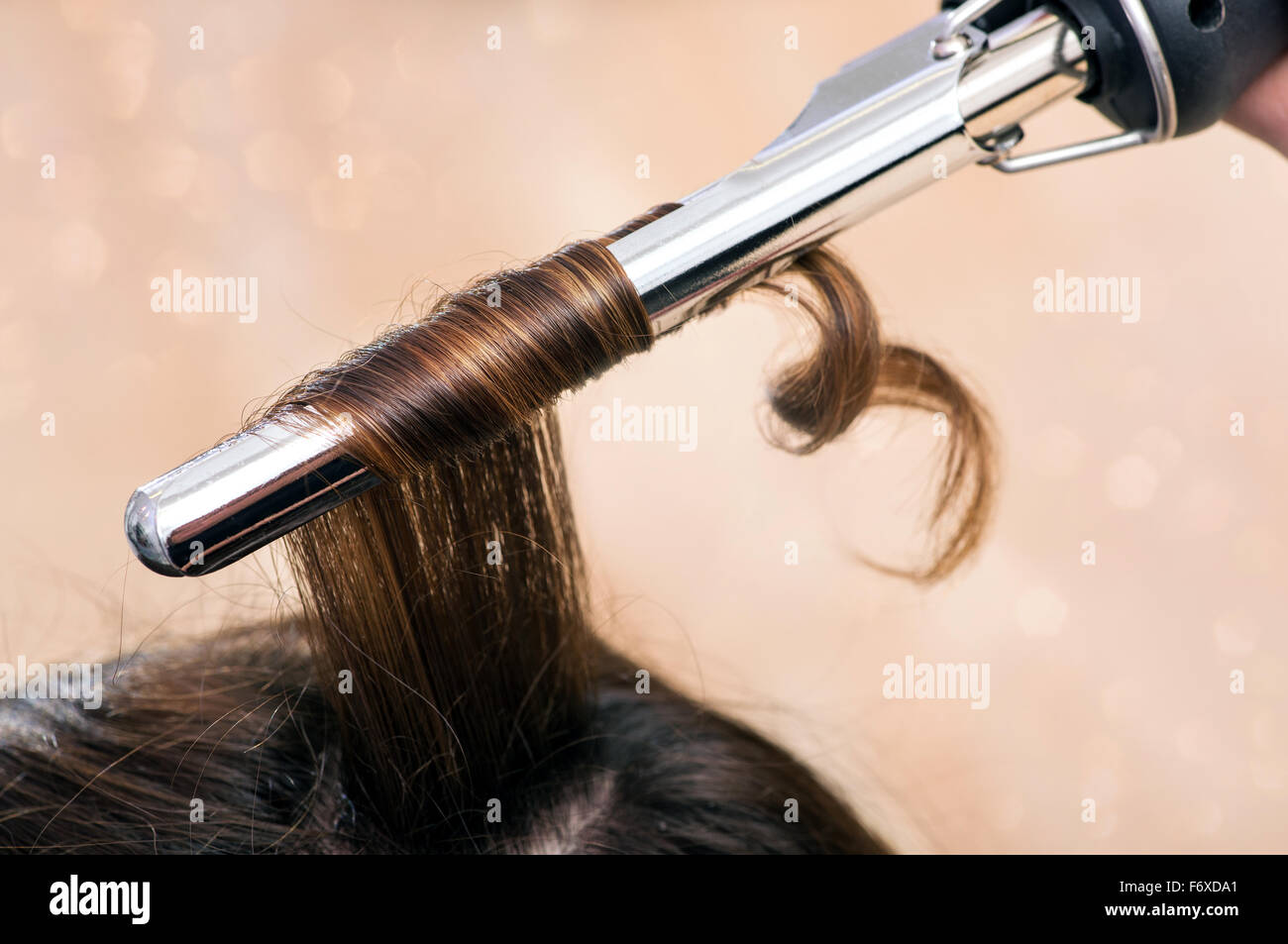 Hairstylist using a curling iron to firm ringlets in the long brown hair of a female client Stock Photo