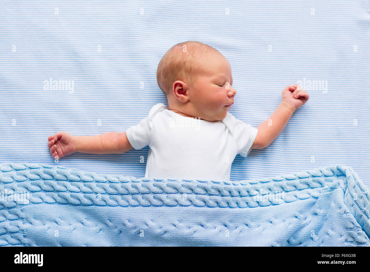 Newborn baby boy in bed. New born child sleeping under a blue knitted blanket. Children sleep. Bedding for kids. Stock Photo