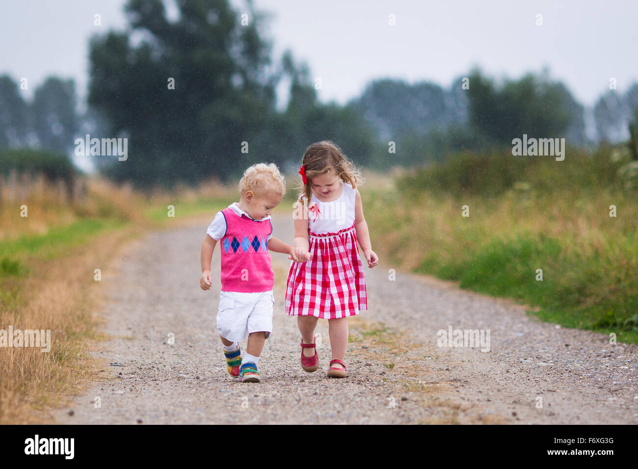 Girl and boy playing in the rain. Kids play outdoor by rainy weather in fall. Autumn fun for children. Toddler kid and baby walk Stock Photo