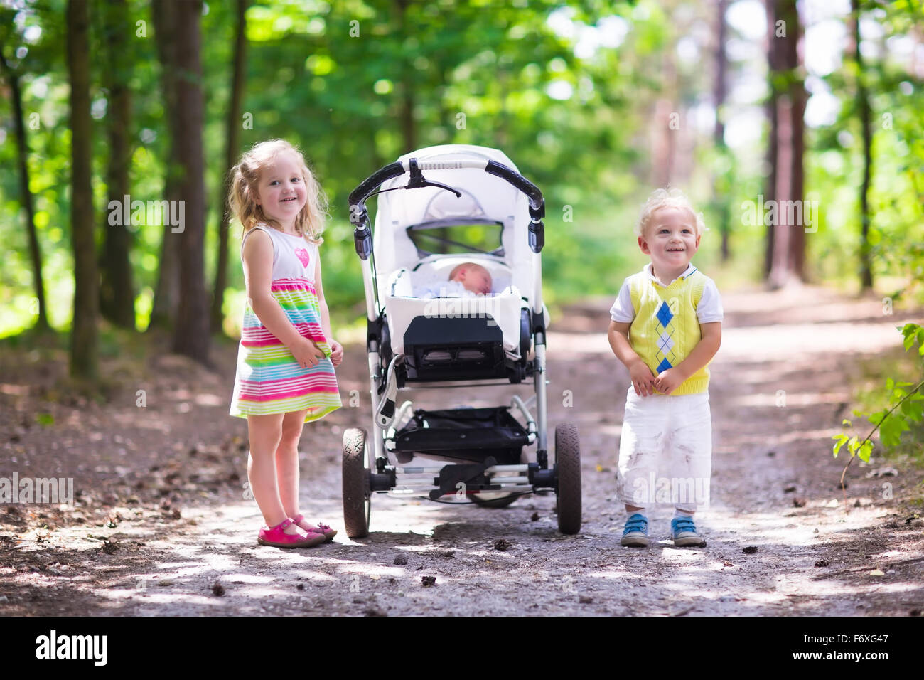 Boy and girl walk in sunny summer park pushing stroller with newborn