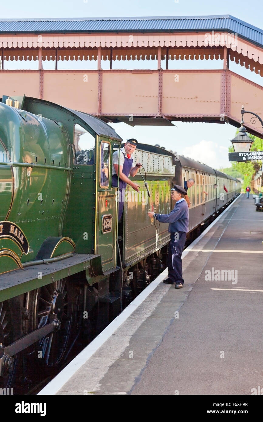 The signalman exchanges a single line token with the fireman of steam train at Williton station on the West Somerset Railway, En Stock Photo