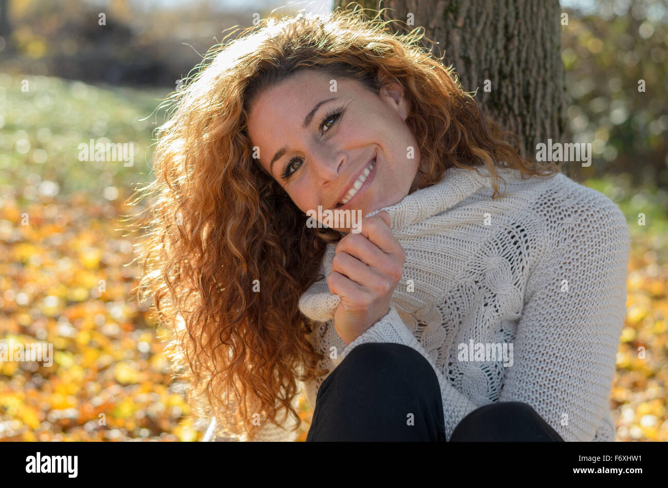 Young woman sitting in front of a tree while looking in to the camera ...