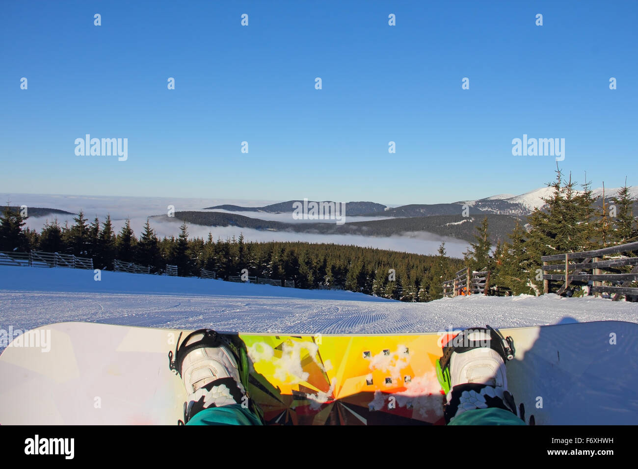 Legs and snowboard od snowboarder sitting on snow with mountains on background Stock Photo