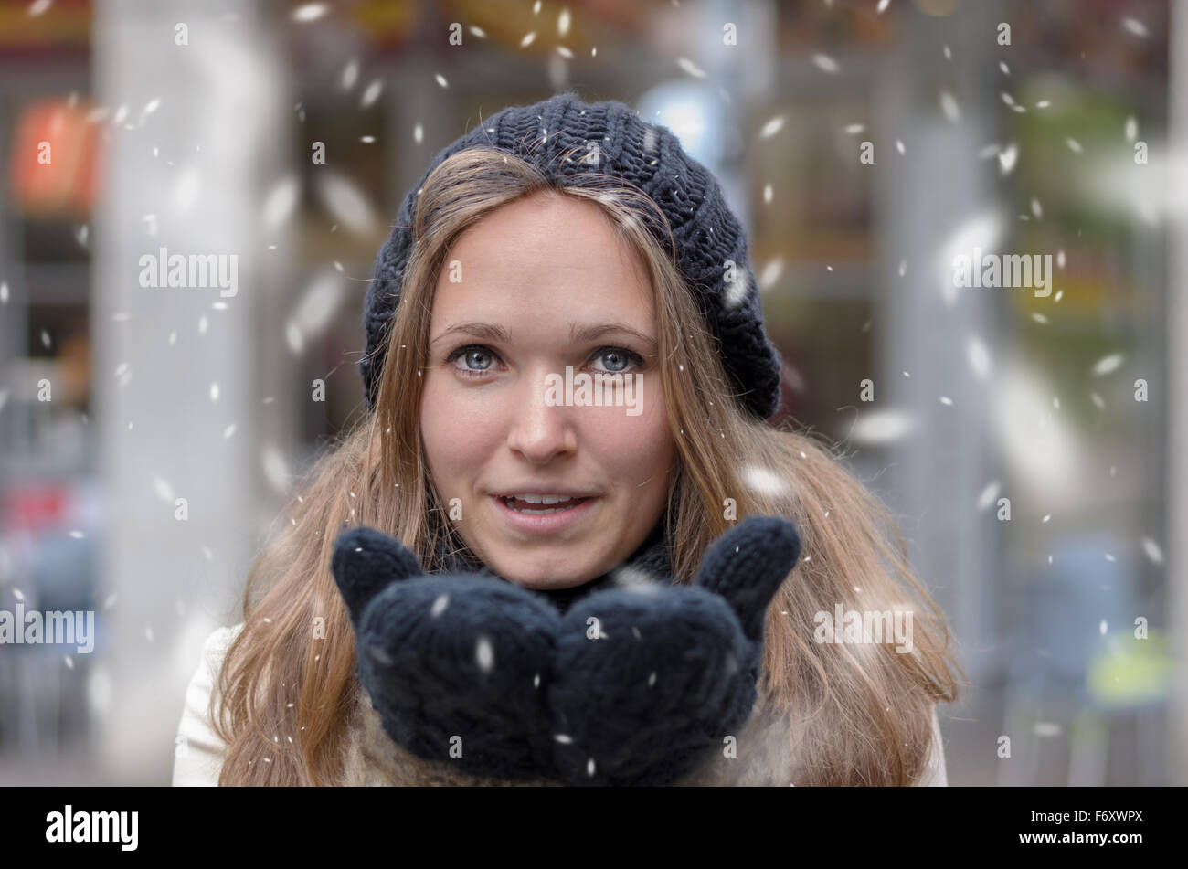 Beautiful girl in fashionable winter clothes blows snow from the