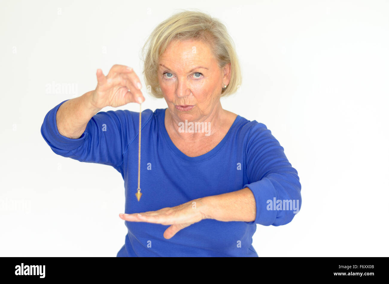 Attractive blond elderly woman holding a pendulum over her hand in a fortune telling, divination or hypnosis concept Stock Photo