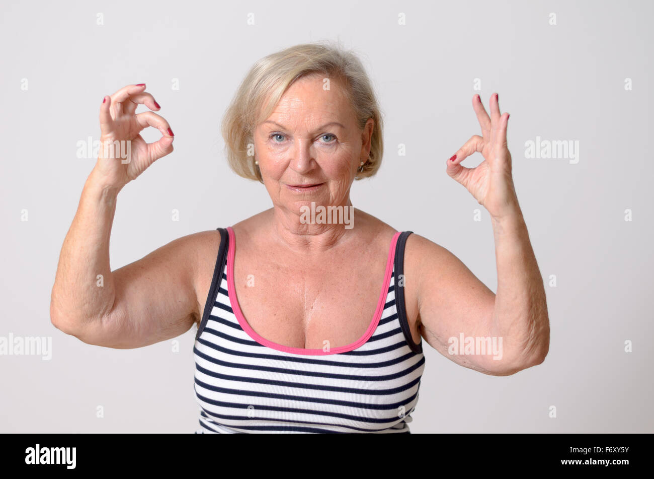 Portrait of a Middle Aged Blond Woman in Casual Striped Shirt, Showing Two Okay Hand Signs While Looking at the Camera. Isolated Stock Photo