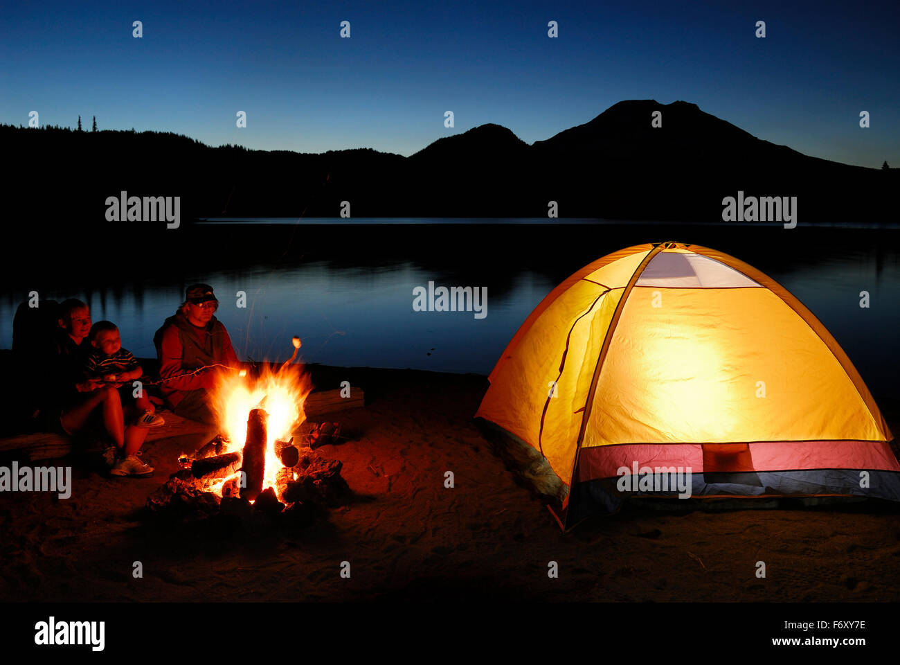 Family roasting marshmallows over a campfire beside Sparks Lake Bend Oregon USA Stock Photo