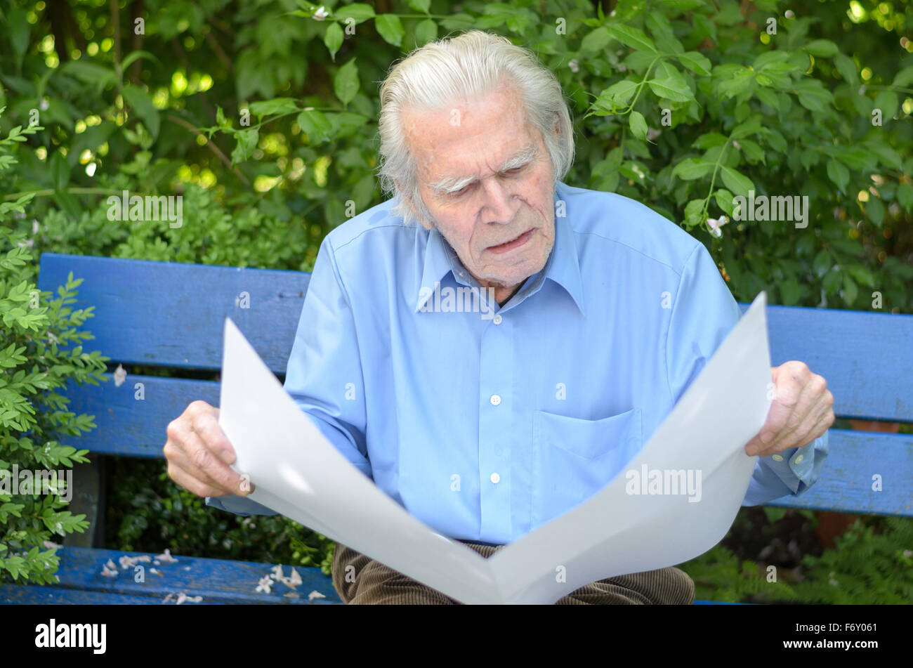 Elderly man sitting alone on a blue wooden bench in the park while ...