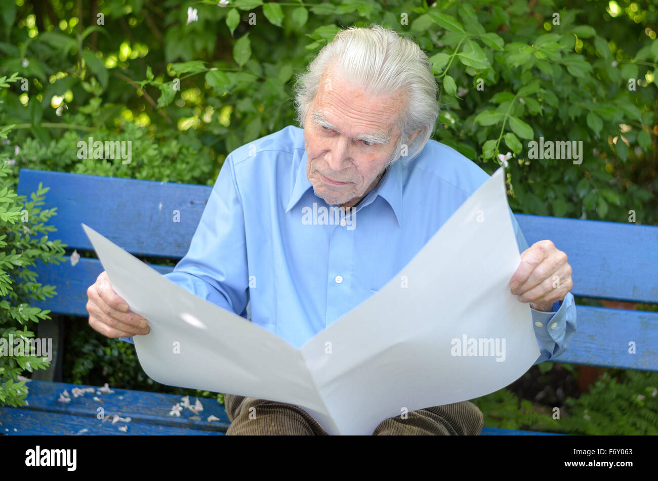 Elderly man sitting alone on a blue wooden bench in the park while ...