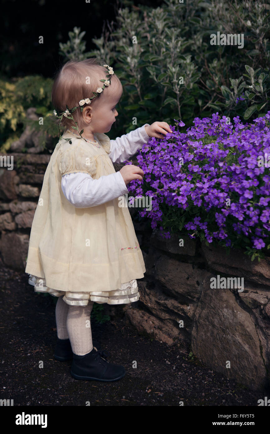 Toddler girl in dress looking at spring flowers in garden Stock Photo